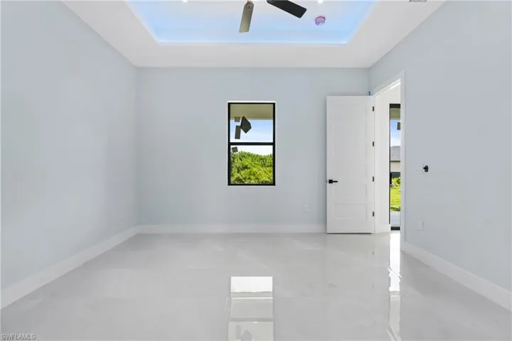 Spare room with light tile patterned flooring, a tray ceiling, ceiling fan, and a healthy amount of sunlight