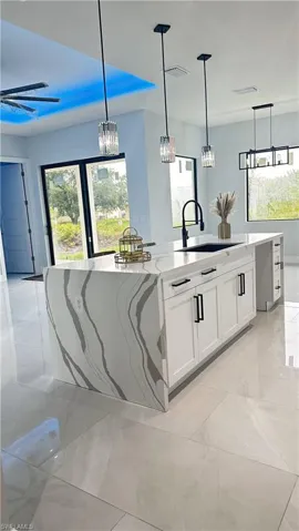 Kitchen with light tile patterned floors, decorative light fixtures, and a center island with sink