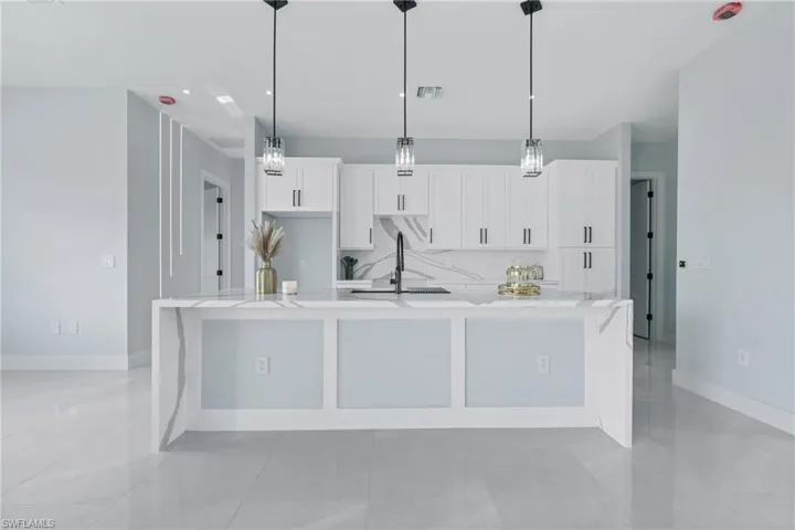 Kitchen featuring light tile patterned flooring, pendant lighting, a center island with sink, and light stone counters