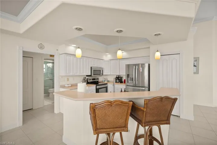 Kitchen with a breakfast bar area, stainless steel appliances, white cabinets, decorative light fixtures, and a raised ceiling