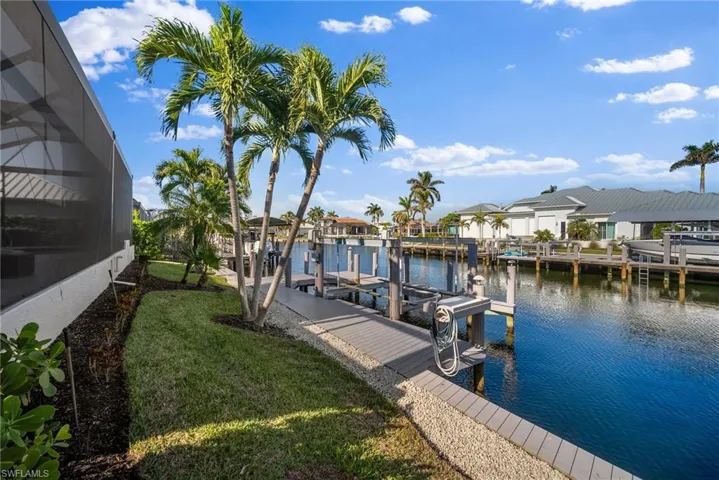 Dock area with a lawn, a water view, and glass enclosure