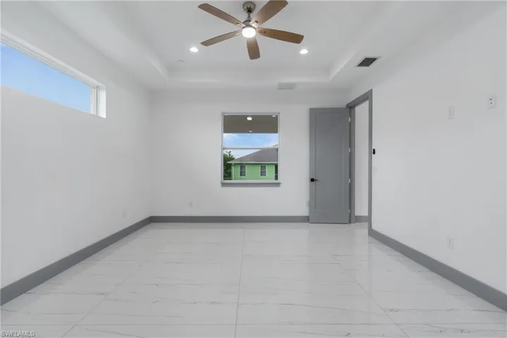 Tiled spare room featuring a healthy amount of sunlight, a raised ceiling, and ceiling fan