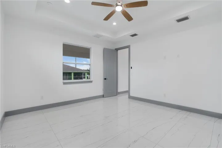 Empty room featuring a raised ceiling, light tile patterned floors, and ceiling fan