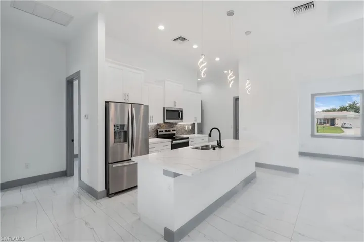 Kitchen with appliances with stainless steel finishes, white cabinets, sink, a kitchen island with sink, and light tile patterned flooring
