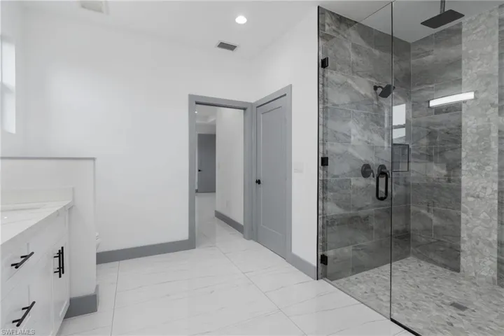 Bathroom with a shower with shower door, tile patterned floors, and vanity