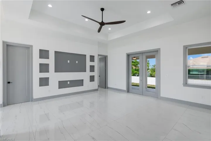 Tiled empty room featuring ceiling fan, french doors, and a tray ceiling