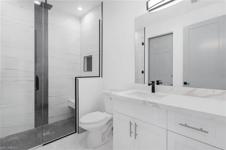 Bathroom featuring a shower with shower door, vanity, tile patterned flooring, and toilet