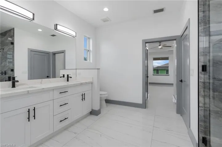 Bathroom featuring toilet, tile patterned floors, ceiling fan, and double vanity