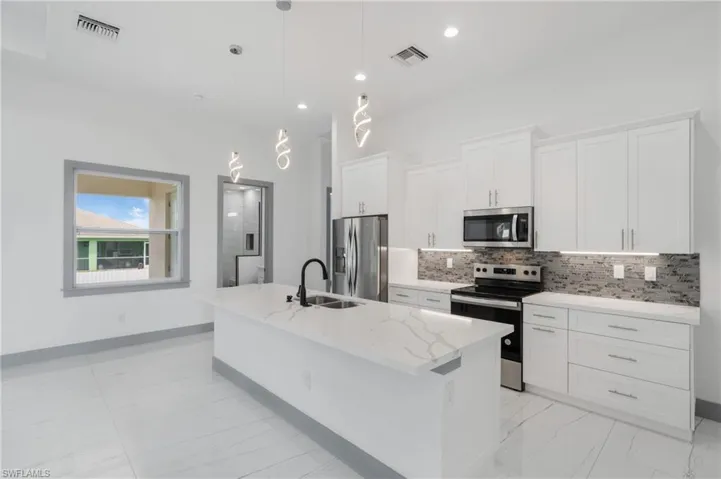 Kitchen with light tile patterned flooring, white cabinetry, light stone counters, stainless steel appliances, and sink
