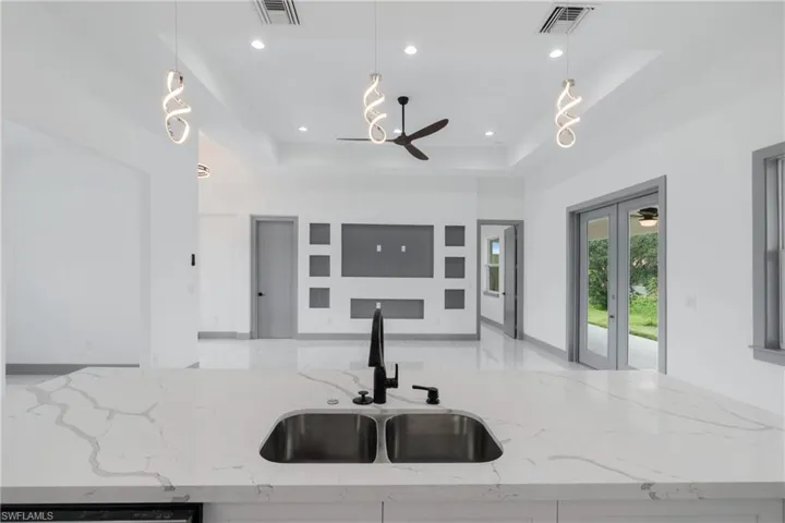 Kitchen featuring sink, light stone countertops, pendant lighting, and a raised ceiling
