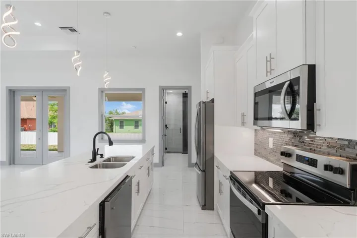 Kitchen with stainless steel appliances, light stone counters, decorative light fixtures, decorative backsplash, and light tile patterned flooring