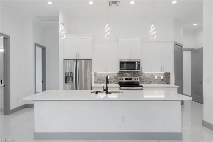 Kitchen with light tile patterned floors, appliances with stainless steel finishes, sink, and an island with sink