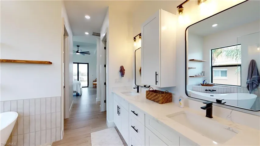 Full bath with double vanity, a freestanding bath, a ceiling fan, recessed lighting, and ensuite bath