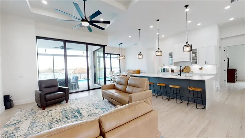 Living room with ceiling fan, recessed lighting, light wood-style floors, a water view, and a towering ceiling