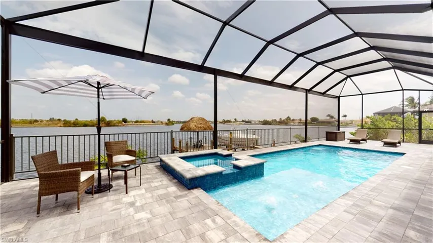 View of swimming pool featuring a pool with connected hot tub, a water view, a patio area, and glass enclosure