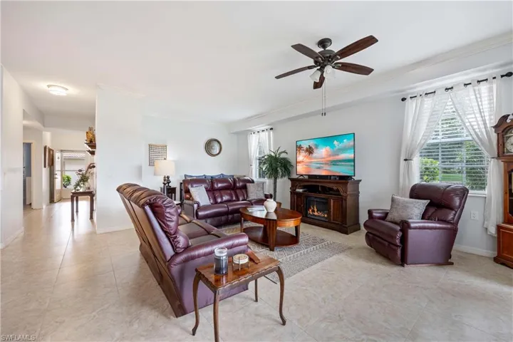 Living area with a lit fireplace, healthy amount of natural light, a ceiling fan, crown molding, and light tile patterned floors