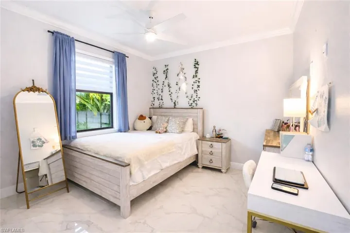 Bedroom featuring light marble finish floors, ornamental molding, and ceiling fan