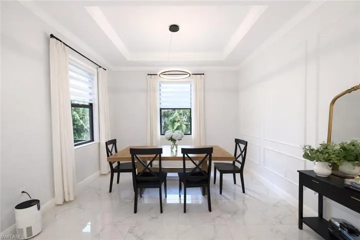 Dining room with a decorative wall, a tray ceiling, light marble finish floors, plenty of natural light, and ornamental molding