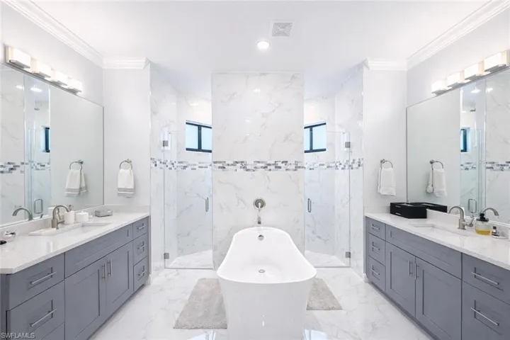 Bathroom with a freestanding bath, crown molding, two vanities, a marble finish shower, and recessed lighting