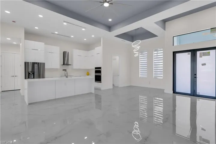 Kitchen with appliances with stainless steel finishes, sink, wall chimney range hood, decorative light fixtures, and white cabinetry