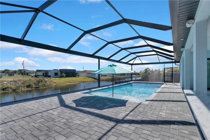 View of pool with glass enclosure, a water view, and a patio