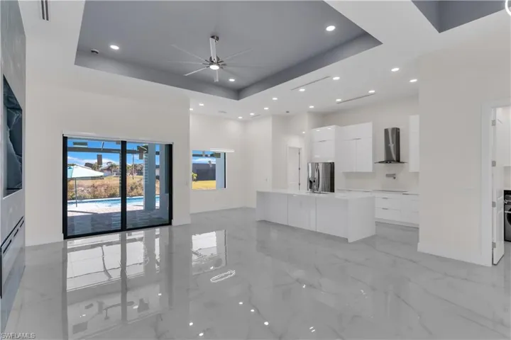 Kitchen featuring white cabinets, a raised ceiling, a kitchen island with sink, and stainless steel refrigerator with ice dispenser