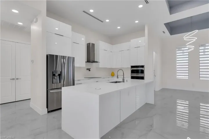 Kitchen with white cabinets, sink, stainless steel appliances, and wall chimney range hood