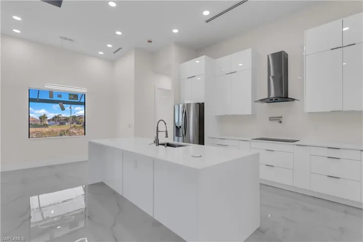 Kitchen with sink, wall chimney range hood, stainless steel fridge, a kitchen island with sink, and white cabinets