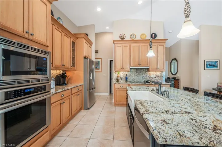 Kitchen with hanging light fixtures, appliances with stainless steel finishes, light tile patterned floors, and backsplash