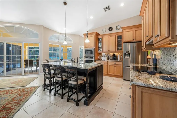Kitchen with light stone counters, hanging light fixtures, a center island with sink, a kitchen breakfast bar, and stainless steel appliances
