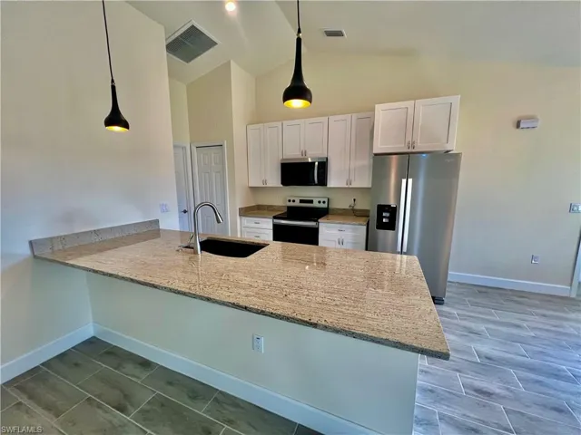 Kitchen featuring sink, white cabinetry, GRANITE COUNTERTOPS WITH BREAKFAST BAR,  a chandelier, and stainless steel appliances