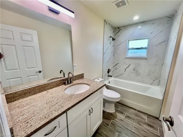 Full bathroom with vanity, tiled shower / bath combo, and toilet