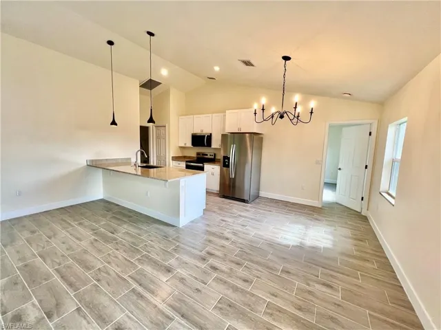 Kitchen featuring appliances with stainless steel finishes, sink, white cabinets, hanging light fixtures, and a notable chandelier