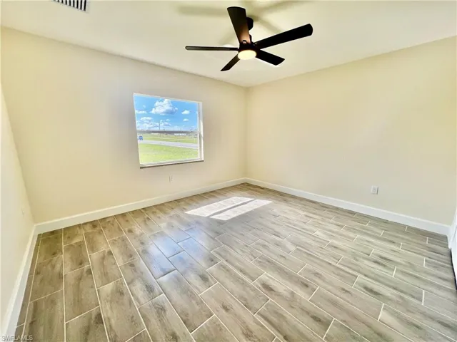Guest bedroom with ceiling fan and wood plank porcelain tile floors.