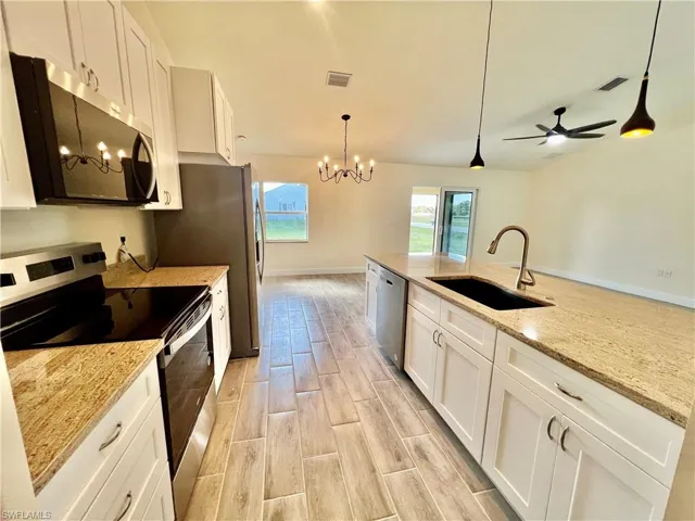 Kitchen featuring sink, white cabinetry, GRANITE COUNTERTOPS WITH BREAKFAST BAR,  a chandelier, and stainless steel appliances