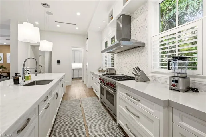 Kitchen featuring light stone counters, white cabinetry, decorative light fixtures, double oven range, and light wood finished floors