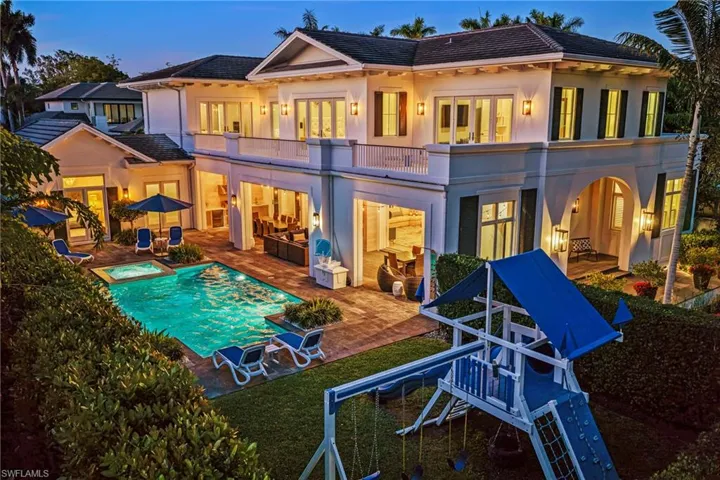 Back of house at dusk featuring a balcony, a patio, stucco siding, a tile roof, and a pool with connected hot tub