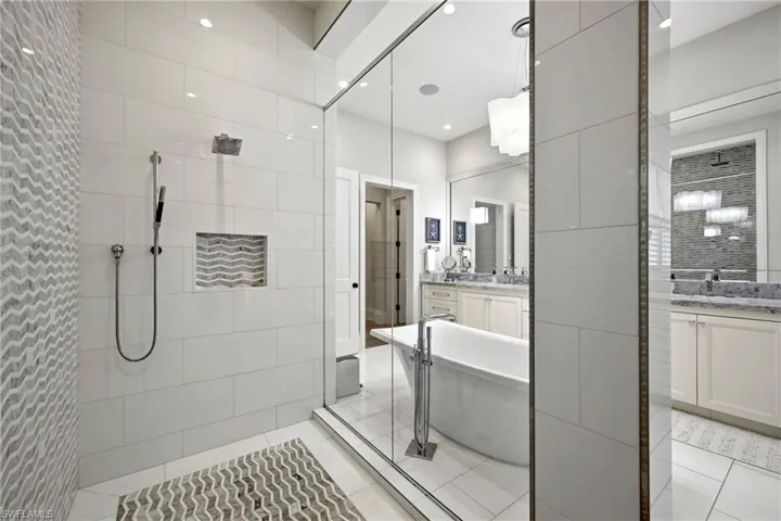 Bathroom with two vanities, walk in shower, a soaking tub, light tile patterned floors, and recessed lighting
