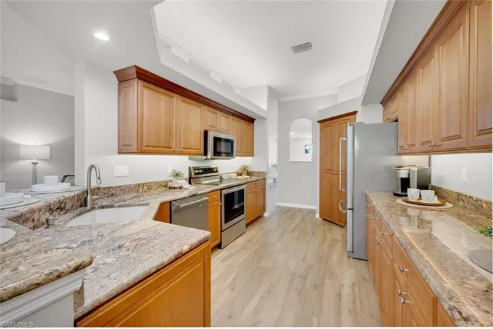 Kitchen featuring stainless steel appliances, sink, light hardwood / wood-style floors, light stone countertops, and crown molding