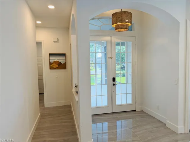 The property entrance features double French doors with transom windows, a modern tiered chandelier, and sleek tile flooring