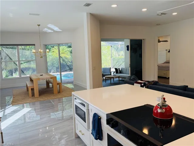 This open-concept living space features light gray tile flooring, a kitchen island with a cooktop and microwave, and large windows with views of a pool