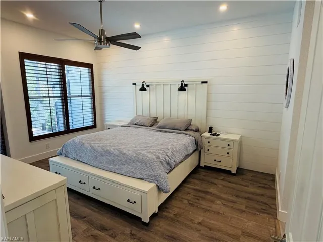 This room features engineered wood flooring, a window with dark wood trim and louvered shutters, and a wall finished with horizontal white paneling