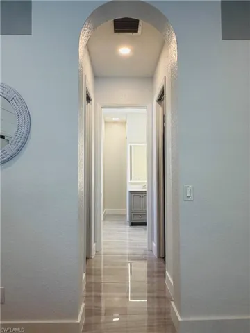 Hallway with a decorative arched entrance, recessed lighting, and glossy flooring