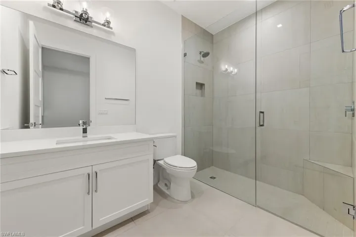 Bathroom with a shower with shower door, tile flooring, vanity, and toilet