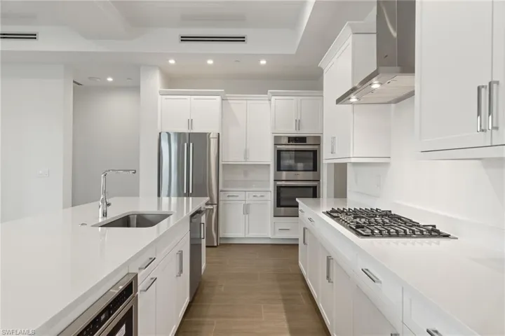 Bosch Kitchen appliances with stainless steel finishes, wall chimney range hood, white cabinets, and deep sink