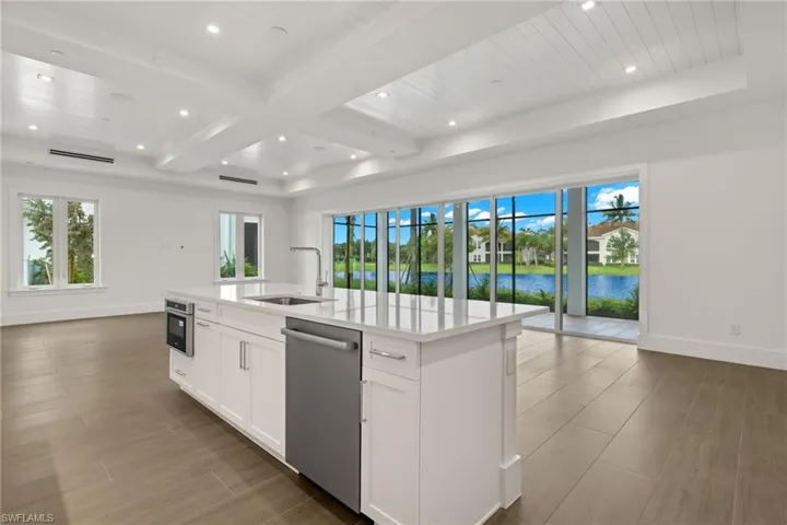 Sun-kissed Kitchen with white cabinetry, a quartz center island with deep sink, stainless steel appliances, beamed ceiling, and a water view