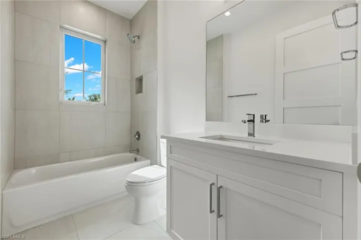 Sun-kissed Full bathroom with tile floors, tiled shower / bath, quartz vanity, and toilet