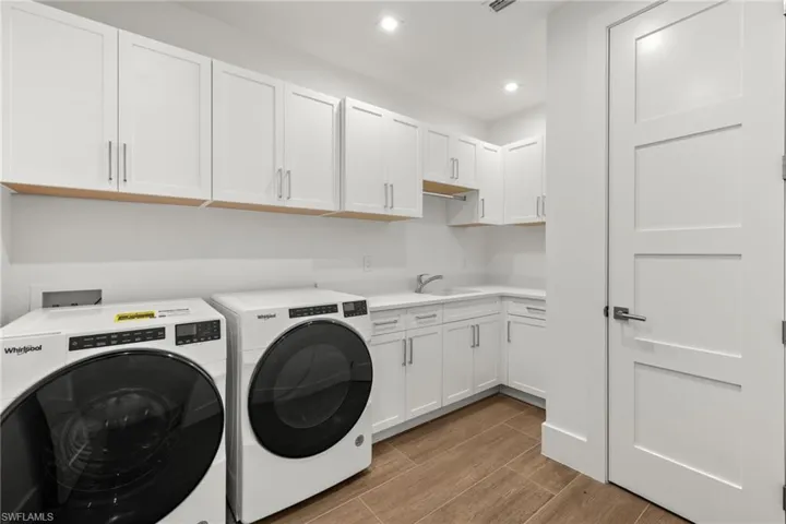Laundry room with cabinets, Whirlpool front loading washing machine and clothes dryer, porcelain tile flooring,  and deep sink