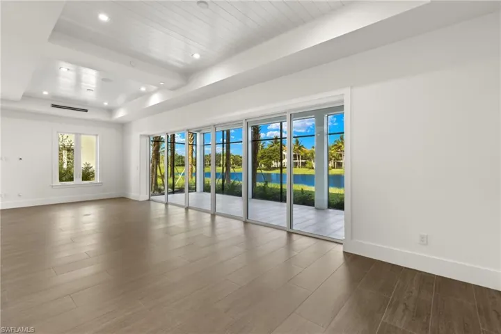 Unfurnished view of great room w/porcelain tile flooring, fabulous, collapsing sliders,  a water view, beam ceiling, and a raised ceiling