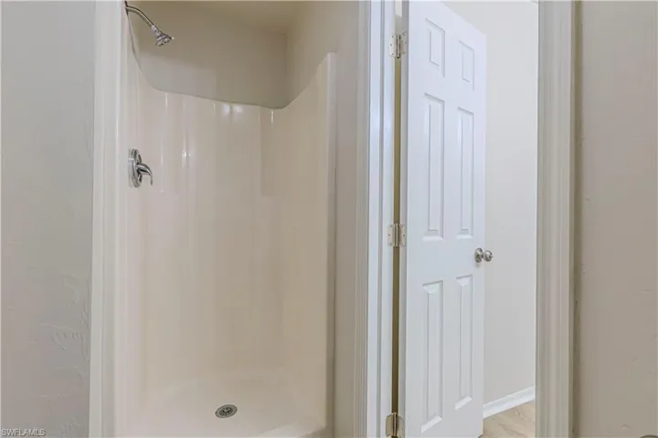 Bathroom with a shower stall, a textured wall, and wood finished floors